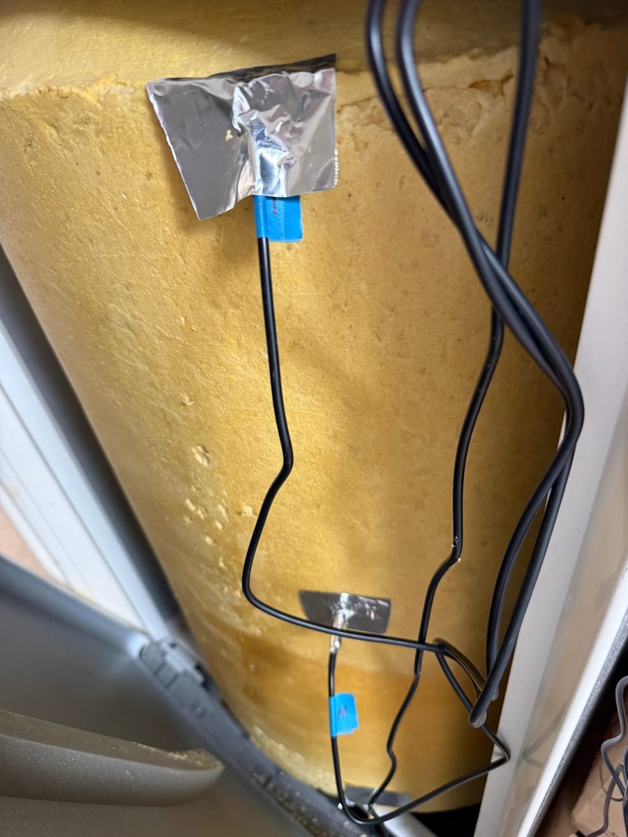 Two of the ten DS18B20 probes clamped against the tank's foam insulation — foil tape for thermal contact, blue tape carrying each sensor's position ID.